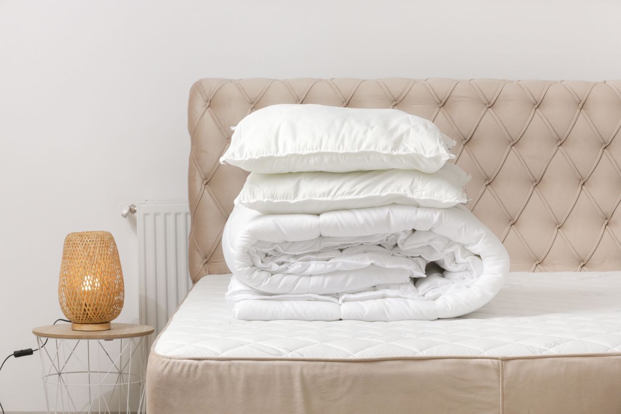 Freshly washed white comforter and pillows stacked on a bed, illustrating clean results after using a laundromat to wash comforters.