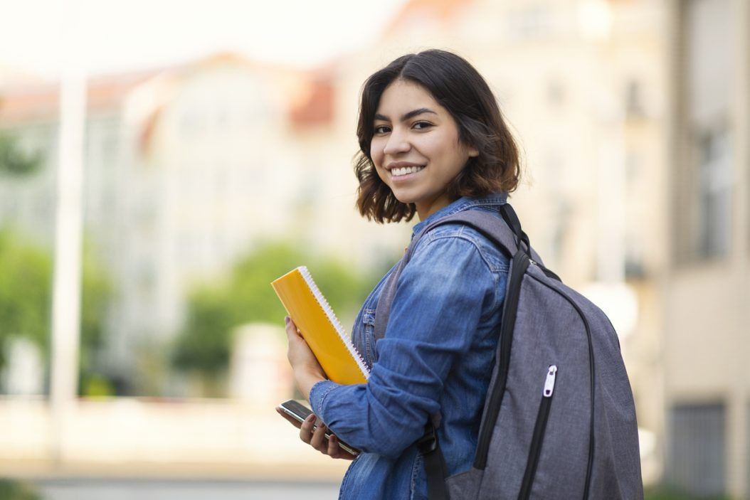 Smiling college student near Nashville laundromat, carrying books and backpack.