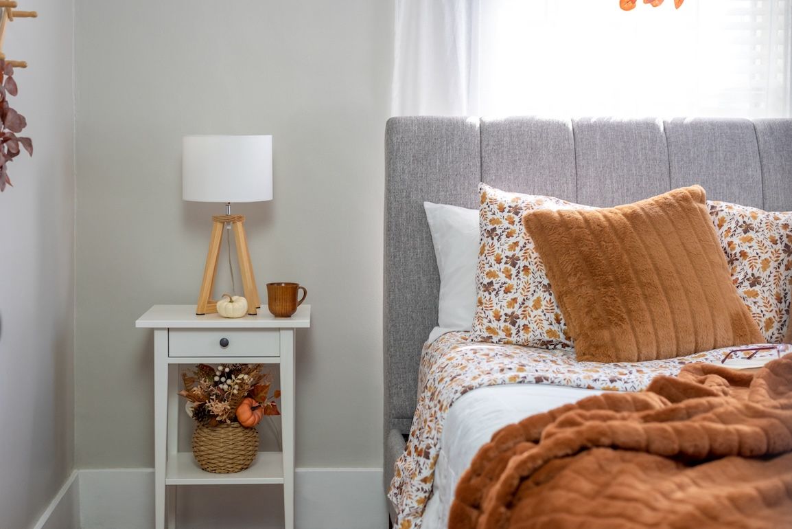 Cozy fall bedroom with gray upholstered bed, white linens, and burnt orange throw pillows, styled with seasonal décor for a warm and inviting look.