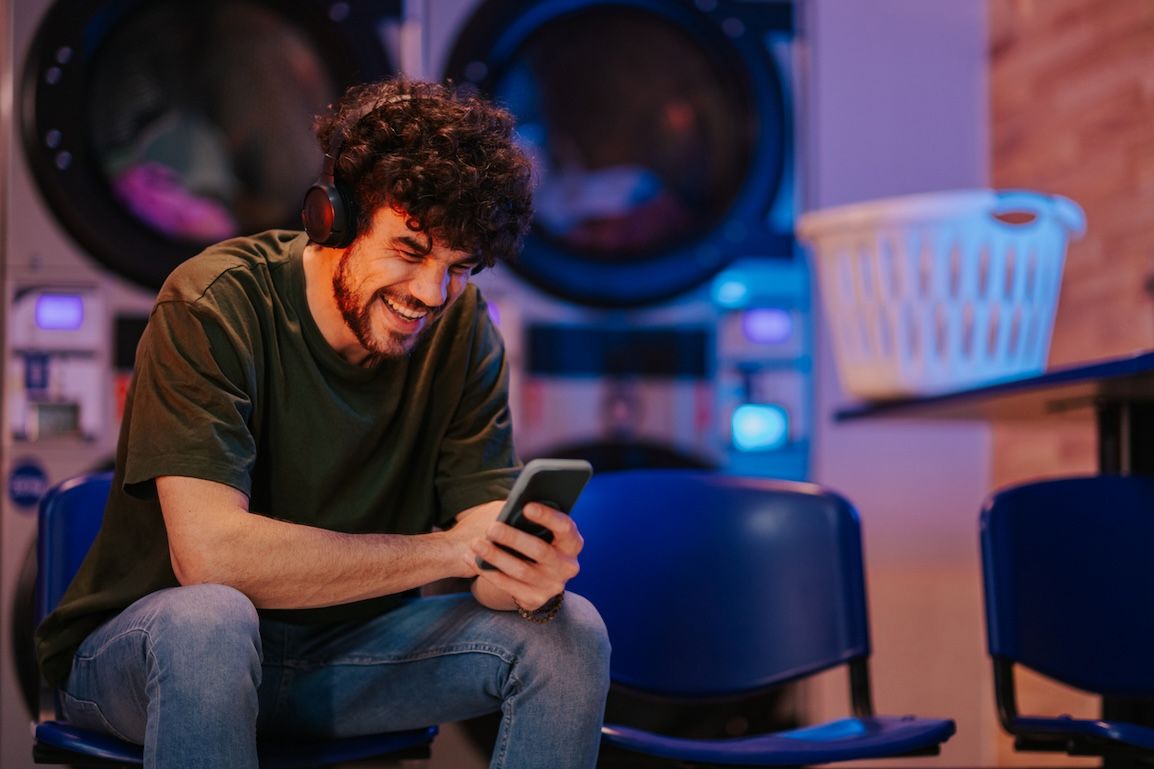 Young man using smartphone at futuristic laundromat with headphones, enjoying smart laundry convenience