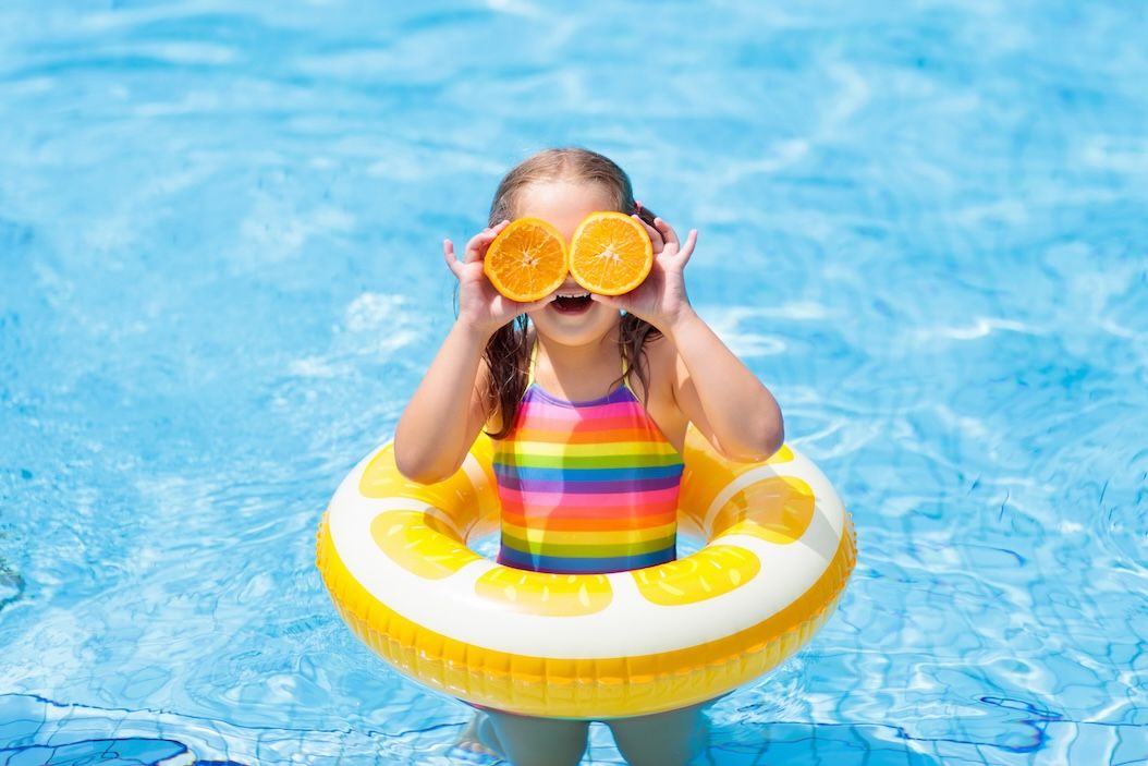 Child in a colorful swimsuit with a lemon float playing in a pool during summer; how to wash swimsuits and extend their life.