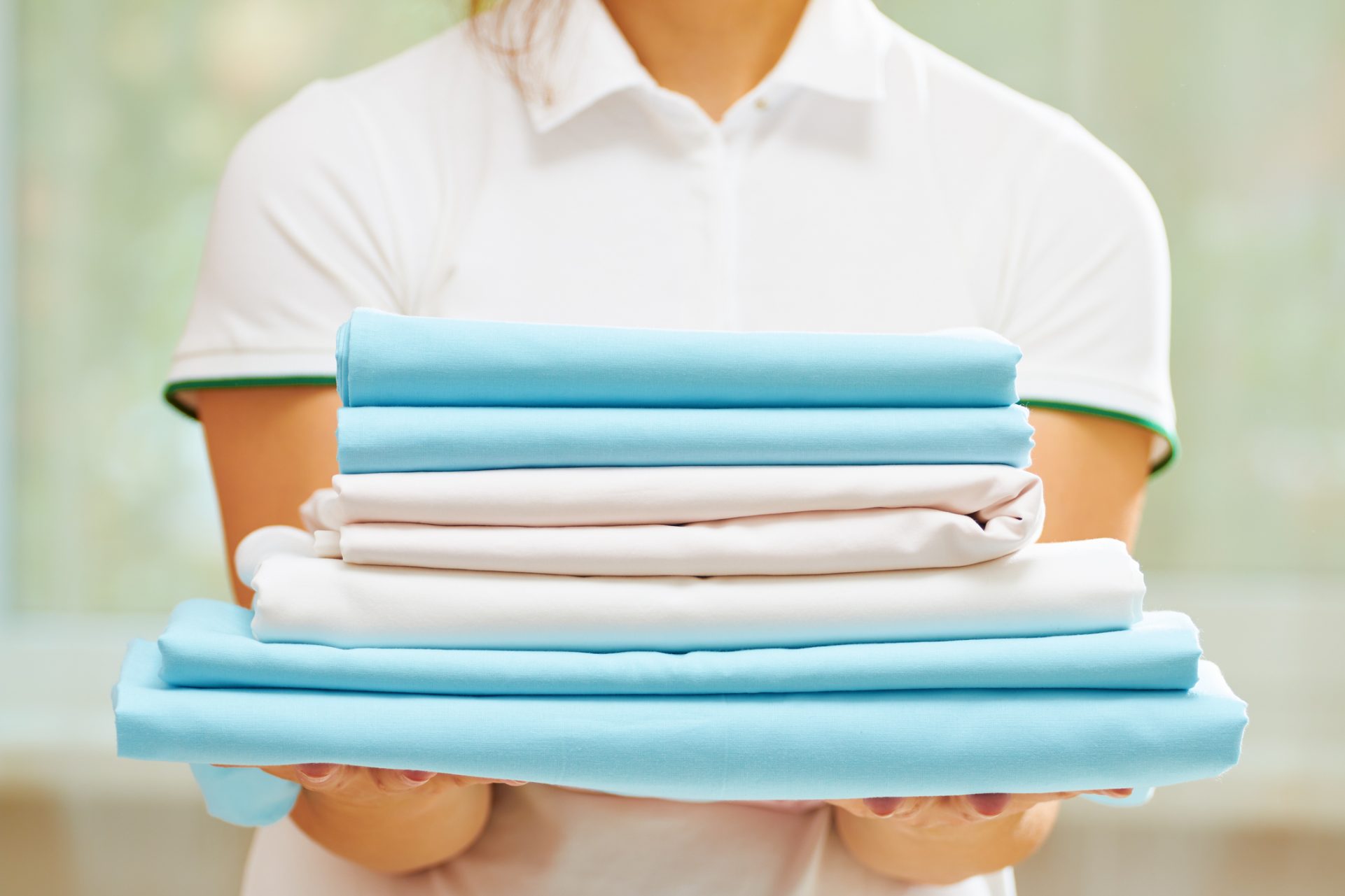 Closeup of woman's hand holding a stack of clean folded linens of blue and white colors.