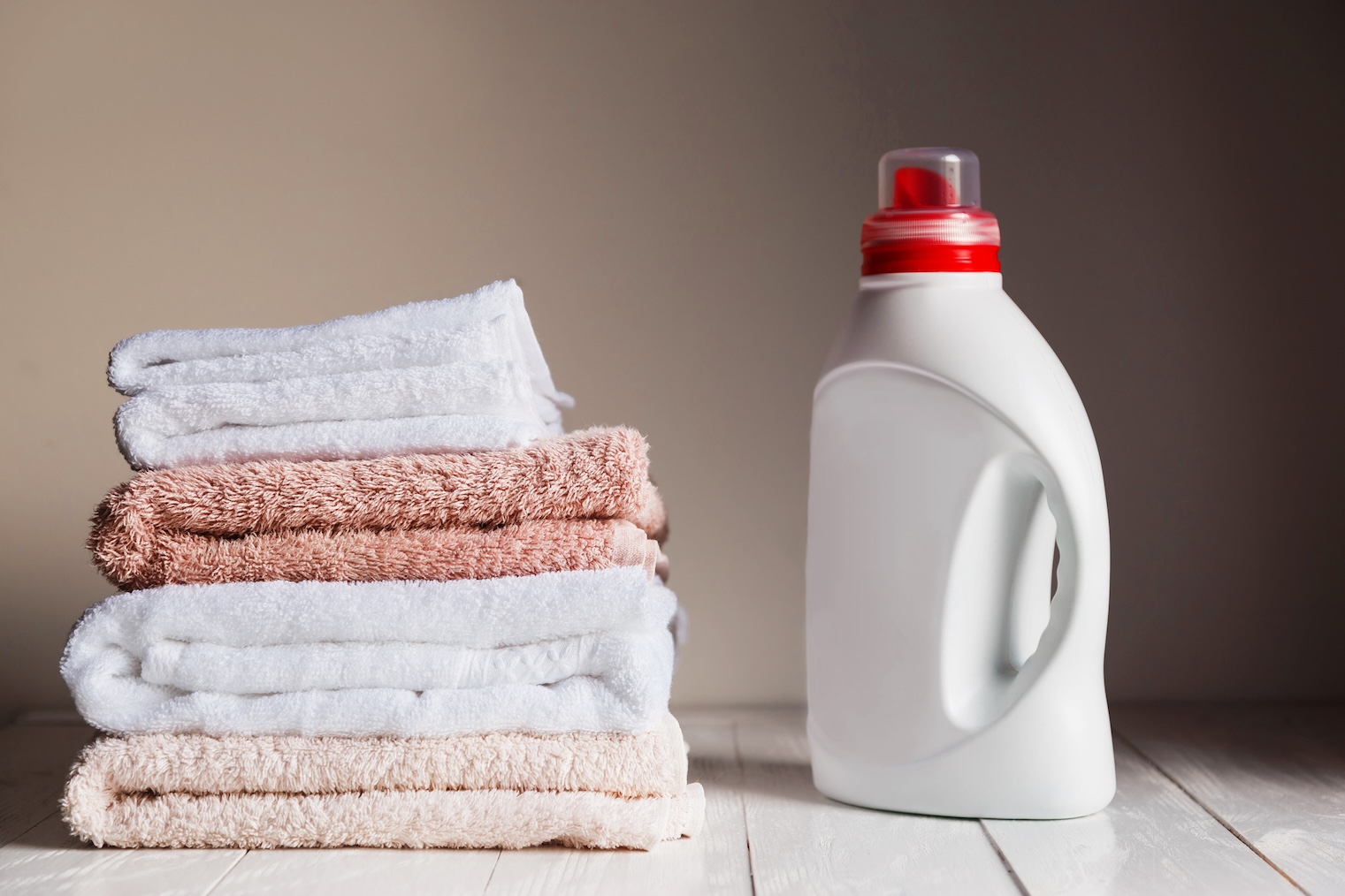 Stack of several pink and white towels and bottle with detergent.