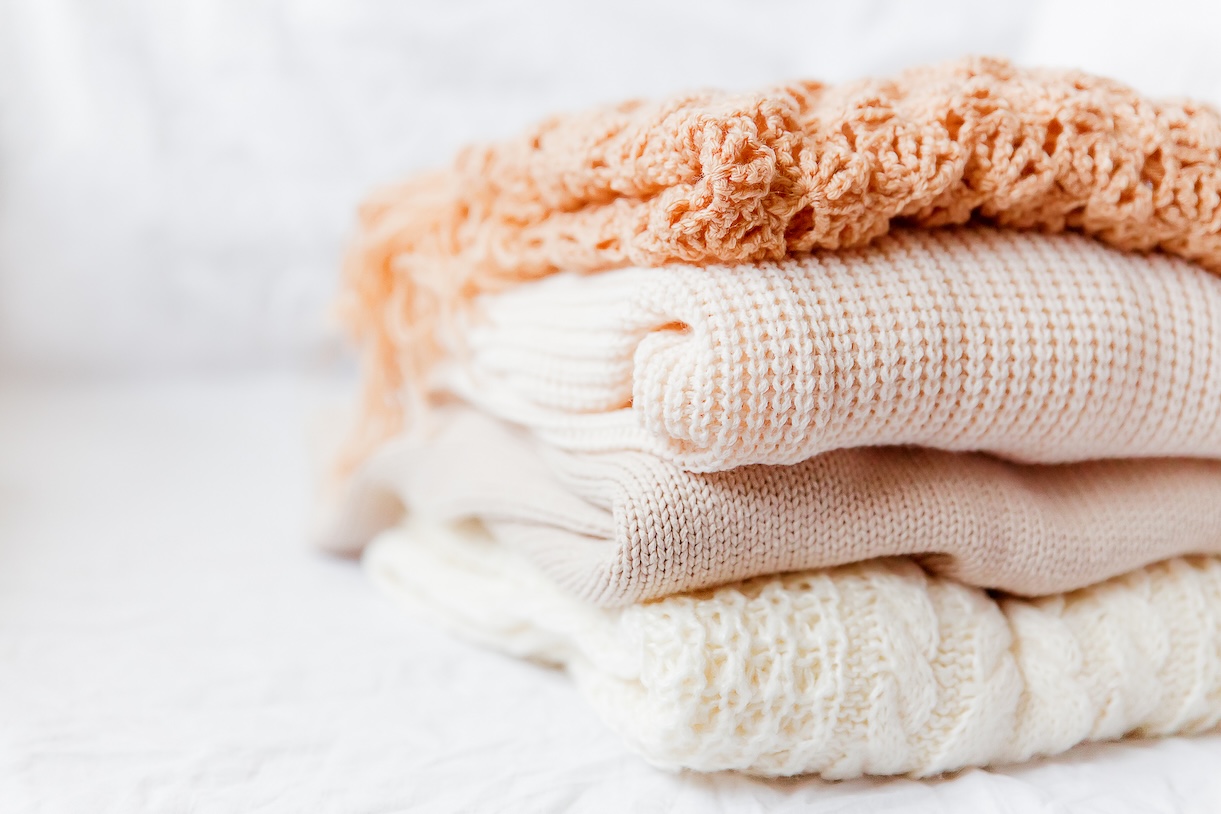 Pile of beige woolen clothes on a white background. Warm knitted sweaters and scarfs are folded in one heap