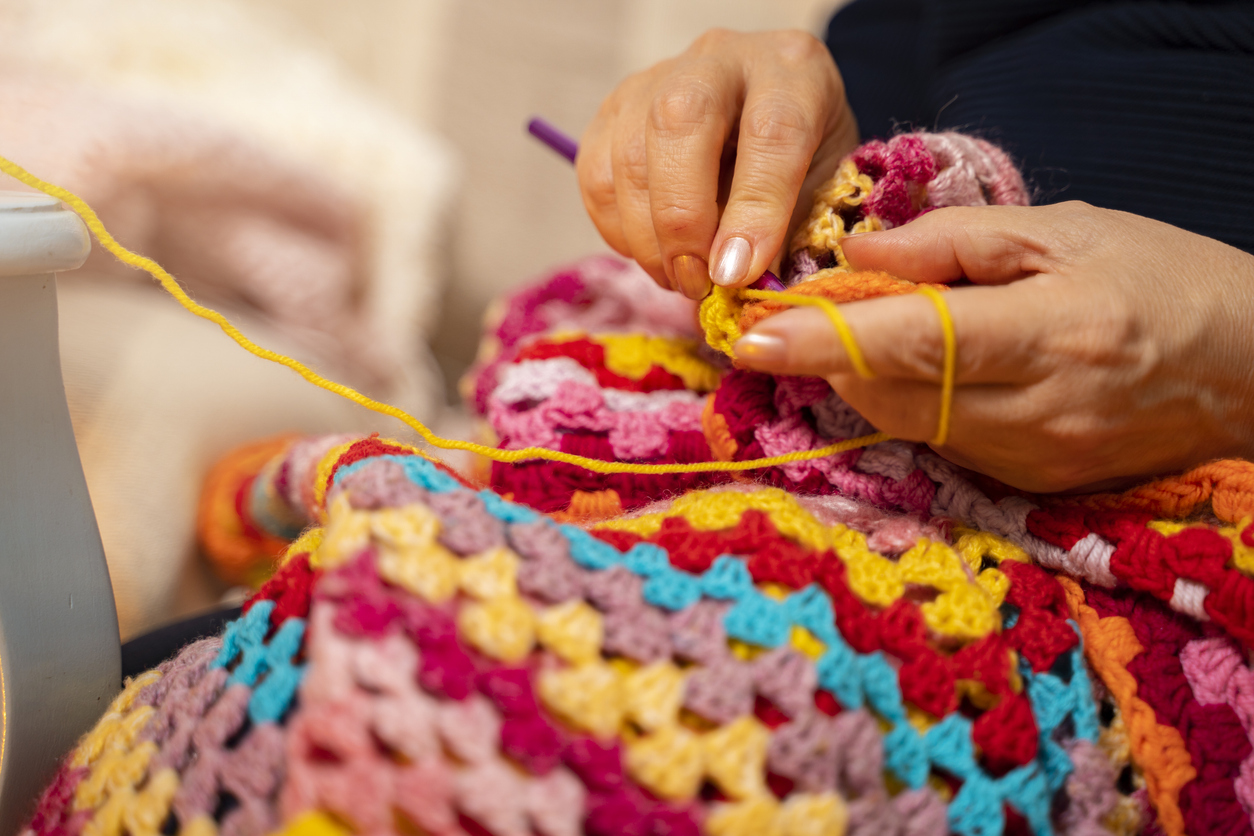 Hands crocheting a colorful blanket.