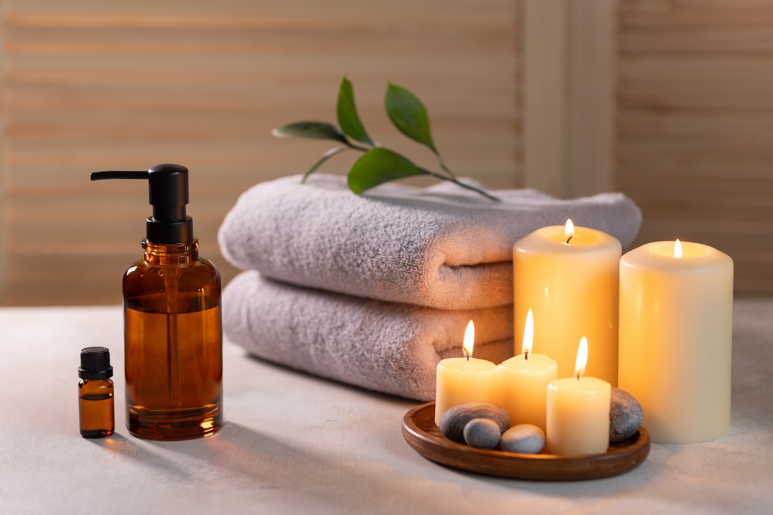 Stacked spa towels with burning candles and essential oil bottles on a table, representing clean linens in a wellness setting.